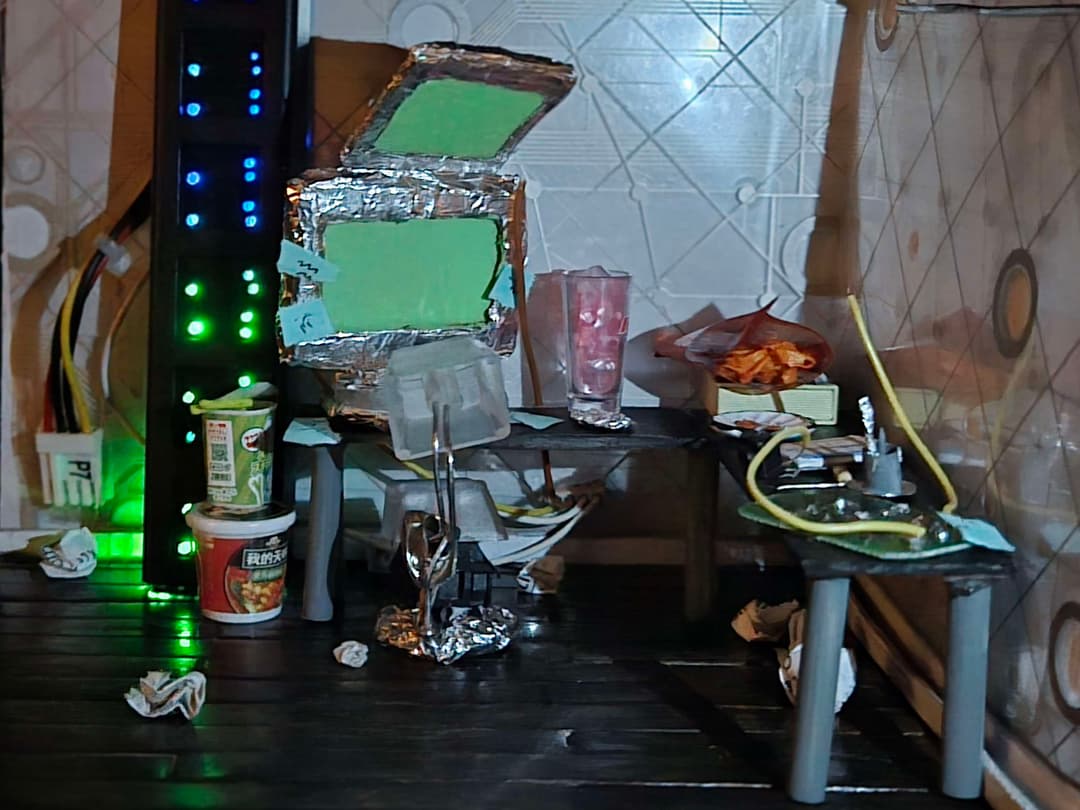 A dimly lit, messy computer room with various electronics and snacks scrambled throughout
